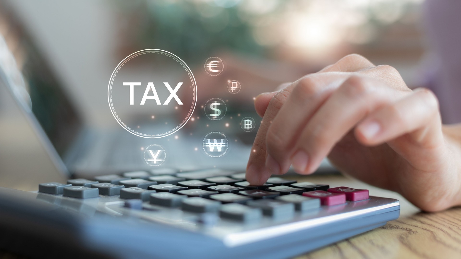 Close-up of a hand using a calculator with a tax icon and global currency symbols, representing international tax planning, finance calculation, and accounting operations.