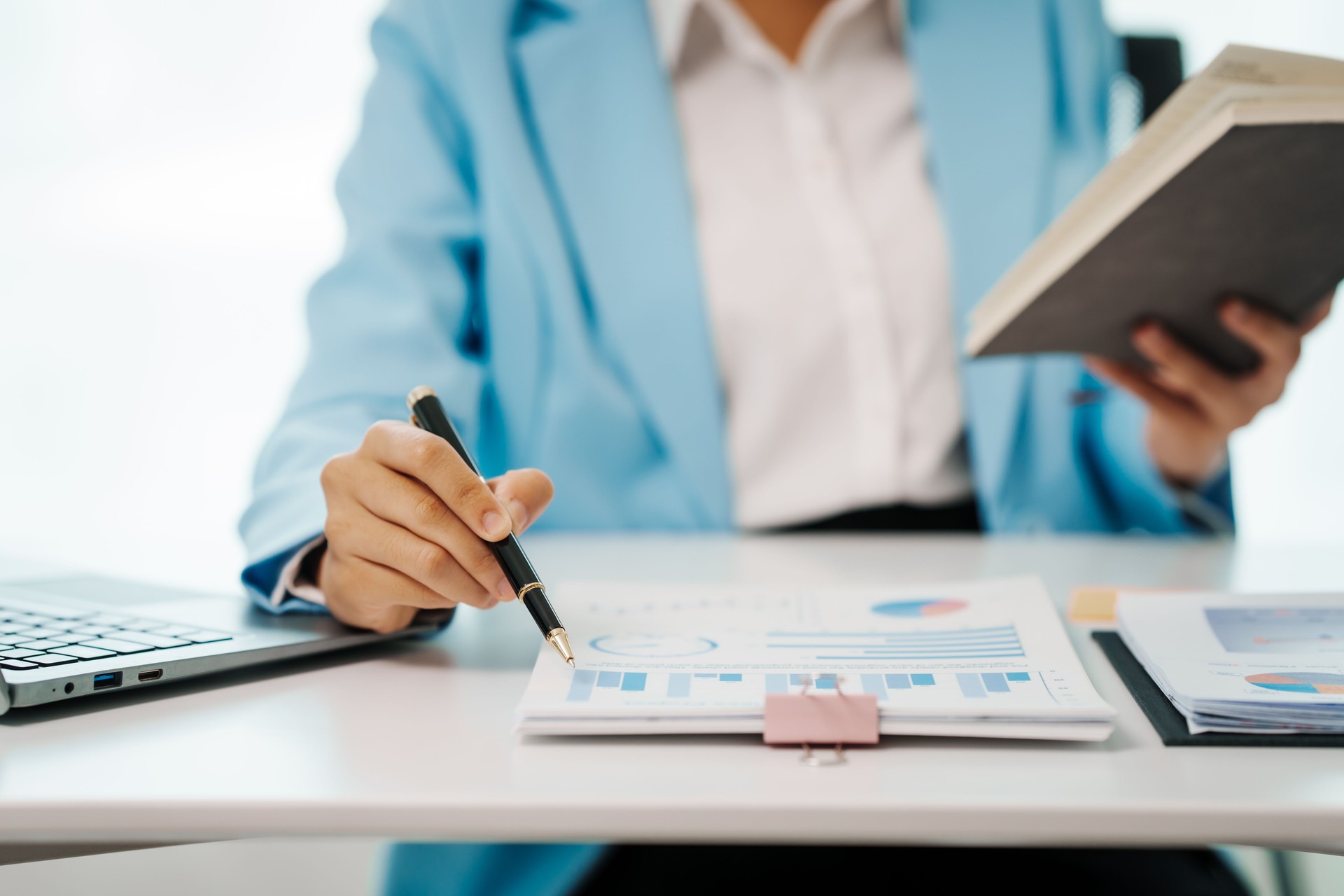 An Asian female accountant works happily at her desk in the office, using a laptop to analyze financial charts. She manages business finance and online transactions for company success An Asian female accountant works happily at her desk in the office, using a laptop to analyze financial charts. She manages business finance and online transactions for company success